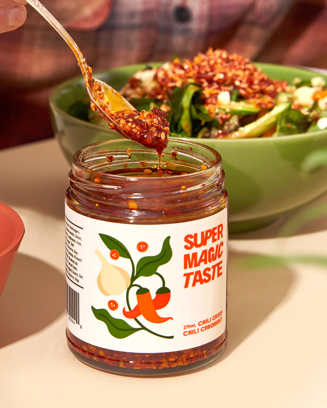 A jar of open Super Magic Taste Chili Crisp and a bowl of salad with Chili Crisp on top